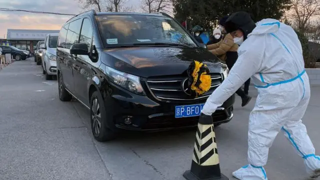 Một nhân viên trong trang phục bảo hộ hướng dẫn xe tang di chuyển vào một nhà tang lễ ở Bắc Kinh hôm 17/12