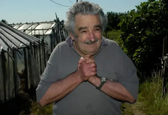 Mujica entrelaçando as mãos. Ao fundo, várias árvores