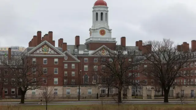 A big white and brown building of Harvard University. For front of am na park and three large trees. 