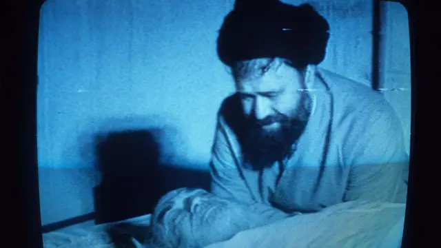 صورة قديمة يظهر فيهها الخميني بعد وفاته: رجل دين بعمامة سوداء - أحمد الخميني - وبجانبه شخص بلحية بيضاء مغمض العينين 