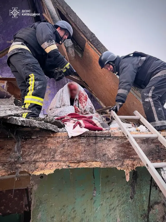 Закривавлена людина із заблюреним обличчям у руїнах будинку та рятувальники