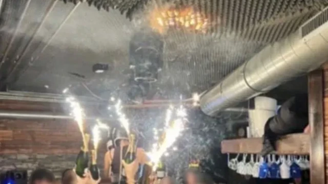На любительском фото - момент начала пожара. Люди у барной стойки тянут руки вверх. В руках - запечатанные бутылки шампанского, а к горлышкам прикреплены горящие бенгальские огни. На потолке виден разгорающийся огонь