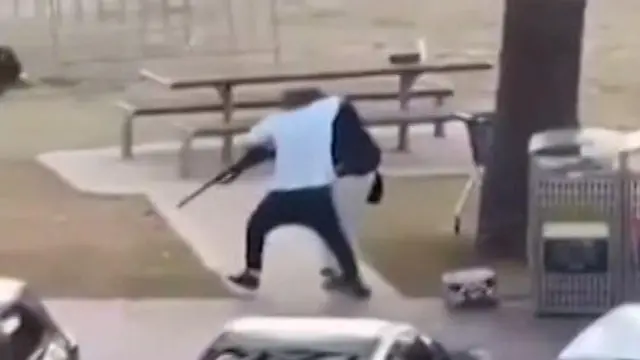 Ifoto igaragaza umugabo wambaye umupira w'umweru w'amaboko magufi arimo kwambura imbunda urimo kurasa. 