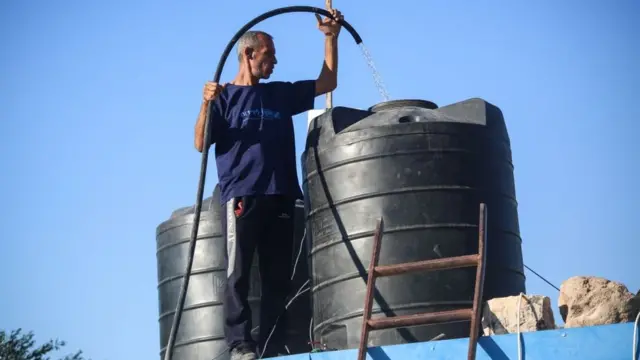 رجل يملأ خزانا بالمياه فوق منزله في غزة