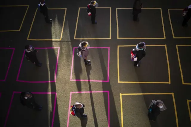 Children stand in social distancing squares on arrival at school.