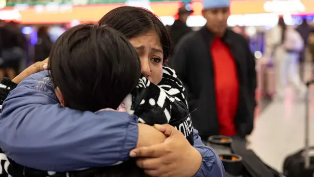 A imigrante equatoriana Andrea, de 28 anos, recebe um longo abraço da sua irmã, de frente para a câmera, antes do seu voo para o Equador no Aeroporto Internacional JFK em Nova York, no dia 26 de outubro de 2025. Andrea e sua prima decidiram se "autodeportar" com seus filhos, depois que seus maridos foram detidos por agentes do Serviço de Imigração e Alfândega dos Estados Unidos (ICE) e deportados para o Equador, por não terem documentos. A filha mais nova de Andrea, Shanell, de 7 meses, nasceu nos Estados Unidos e é cidadã americana.