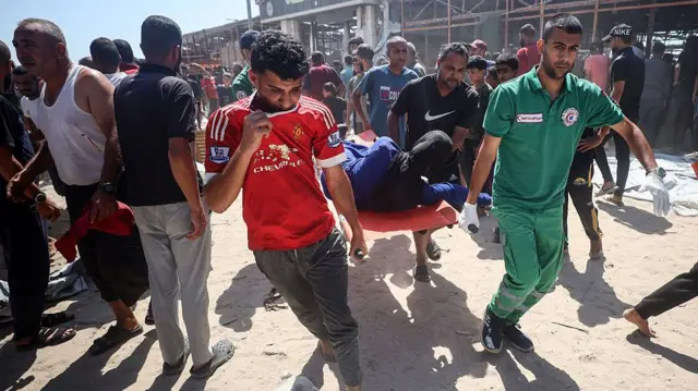 فلسطينيون يحملون مصابا خارج مقهى الباقة بعد استهدافه بغارة جوية إسرائيلية في غرب مدينة غزة، في 30 يونيو/حزيران 2025.