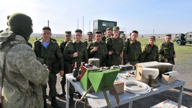 Группа мобилизованных стоит около стола с оборудованием