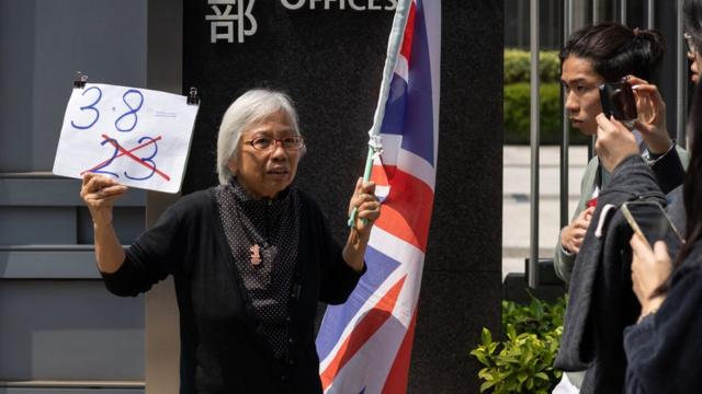香港示威常客「王婆婆」王鳳瑤在中國香港特區政府總部外揮舞英國國旗與自製標語（8/3/2024）