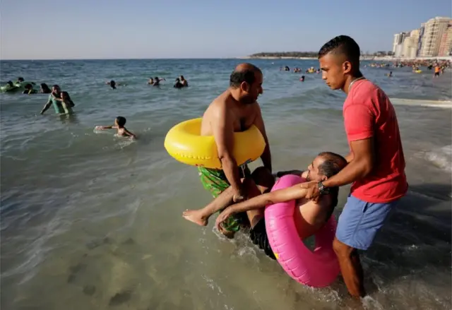 Beach workers help a man to get into the sea.