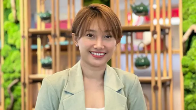 Merisha Ayu, berambut pendek berwarna cokelat terang, memakai lipstik warna merah dan mengenakan blazer hijau sage, berpose tersenyum ke arah kamera. Dia adalah CEO Uji Matcha, kafe matcha yang sudah ada sejak 2017.