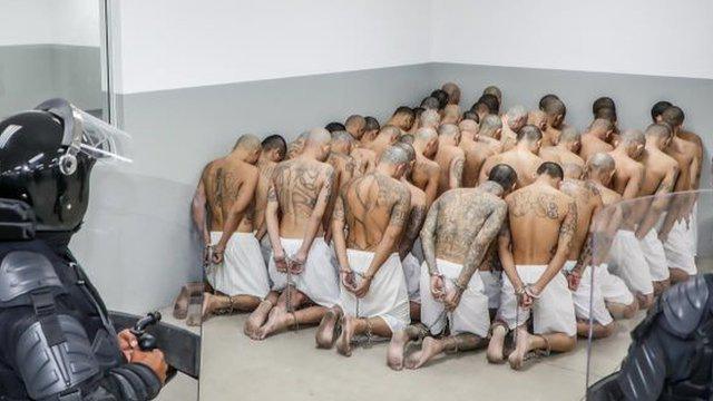 Detidosbetano como funcionacostas, com as mãos para trás e emparedados, com policiais monitorando