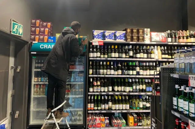 Un employé range des bouteilles de bière dans un magasin d'alcools