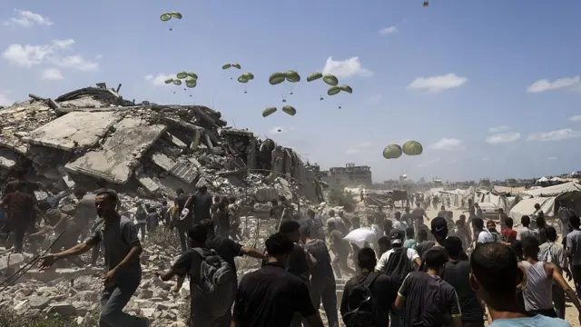 Aviões lançam pacotes de ajuda humanitária por paraquedas enquanto palestinos se aglomeram na área onde os pacotes caem, a oeste da cidade de Gaza.