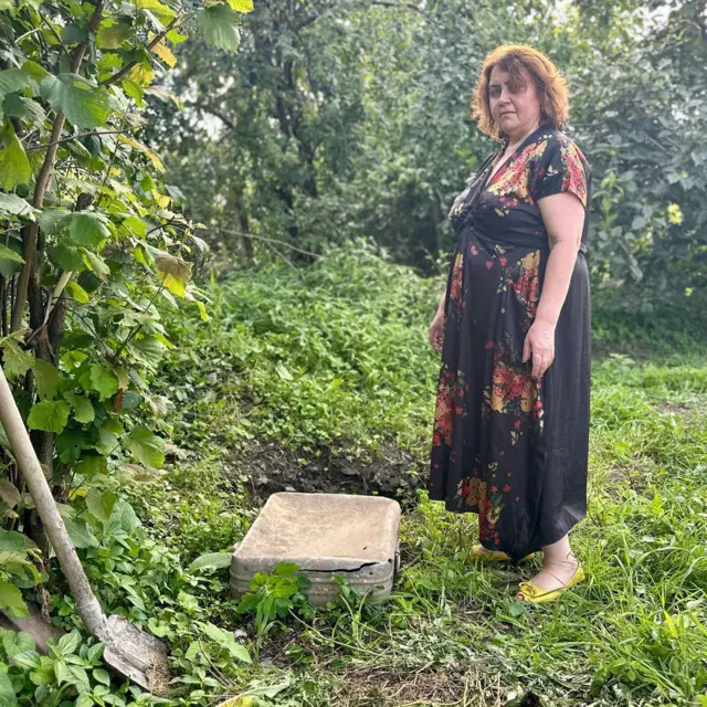 Putri Irina, Nino Elizbarashvili, berdiri di samping koper dan sekop di taman