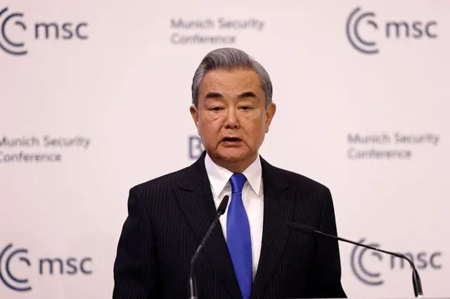 Wang Yi, üzerinde bir takım elbiseyle Münih Güvenlik Konferansı'nda konuşurken. Önünde iki mikrofon, arkasında ise konferansın logoları görülüyor