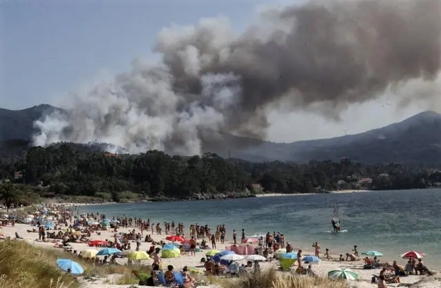 La fumée s'élève d'un feu de forêt près d'une plage touristique
