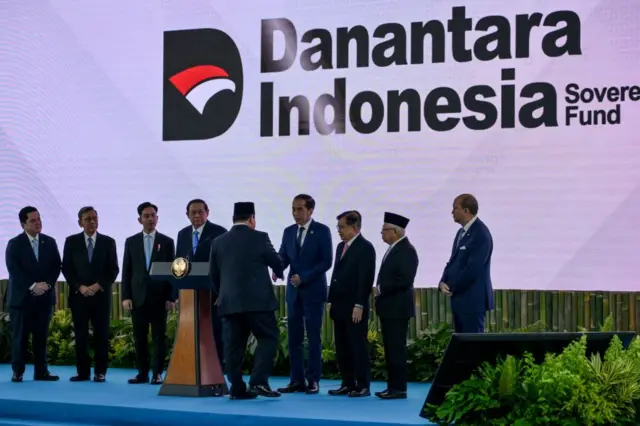 Presiden Indonesia Prabowo Subianto (tengah) berjabat tangan dengan mantan presiden Joko Widodo di atas panggung saat peluncuran BPI Danantara di Jakarta pada 24 Februari 2025.