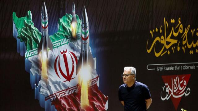 Hombre delante de un cartel en la calle con un mapa de Irán y misiles saliendo de él.