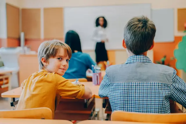 Um menino se vira para olhar para trás na sala de aula.