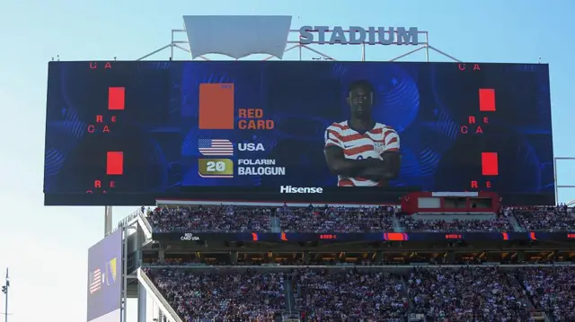 Pantalla gigante de un estadio que muestra una tarjeta roja a Folarin Balogun durante el partido de treintaidosavos de final del Mundial 2026 entre Estados Unidos y Bosnia-Herzegovina, ante miles de espectadores en las gradas.
