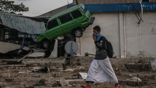 ধ্বংসস্তুপে আটকে থাকা একটি গাড়ির পাশ দিয়ে যাচ্ছেন নাকে কাপড়-দেয়া এক ব্যক্তি
