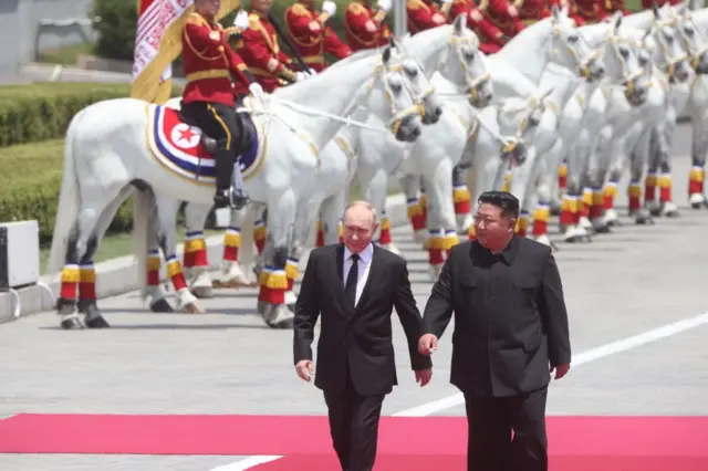 Kim Dzong Un i Władimir Putin idą razem po czerwonym dywanie. 