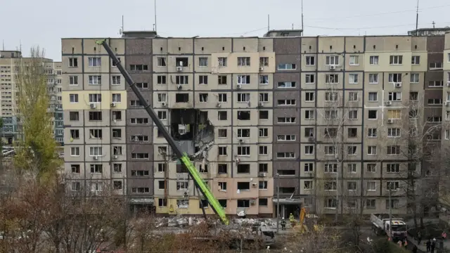 Многоэтажный дом, в который попал беспилотник, и спасательные службы перед зданием.