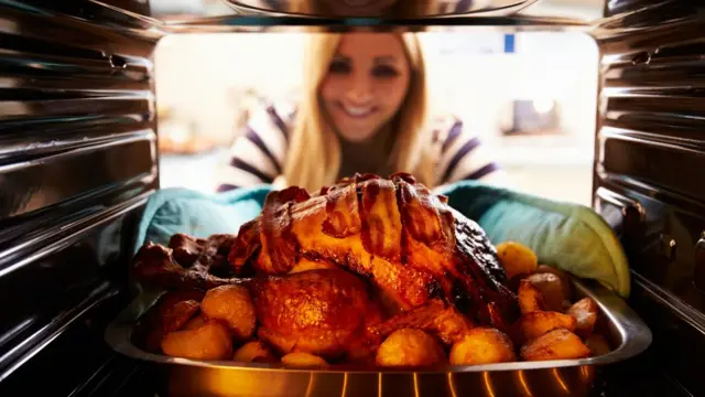 Женщина вытаскивает из духовки индейку