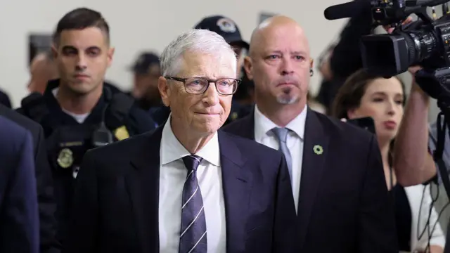 Bill Gates con traje oscuro y camisa blanca, seguido por varios hombres y una muer con gesto serio