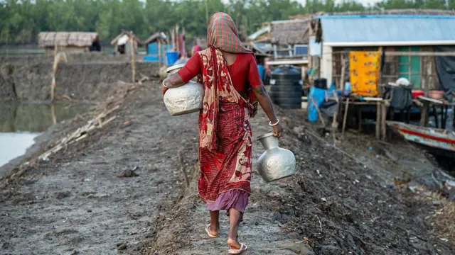 Una mujer con un vestido rojo y un recipiente en busca de agua potable.