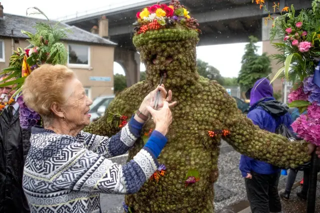 Burryman Andrew Taylor is given whisky through a straw by local resident Mary Hamblin