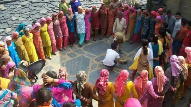Dezenas de mulheres e alguns homens da comunidade hatti, vestidos com roupas coloridas, formam um círculo em volta de dois homens tocando tambores