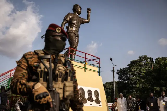 Un militaire avec une arme devant la statue en bronze de Thomas Sankara
