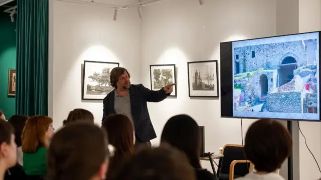 Мужчина стоит перед экраном на фоне рядов слушателей