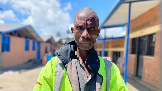 Umugabo uhagaze wambaye ijaketi iriho amabara y'umuhondo. 