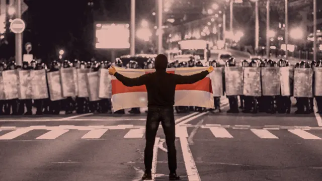 A lone protester holding an old white-and-red flag of Belarus, standing in front of a special forces cordon.
