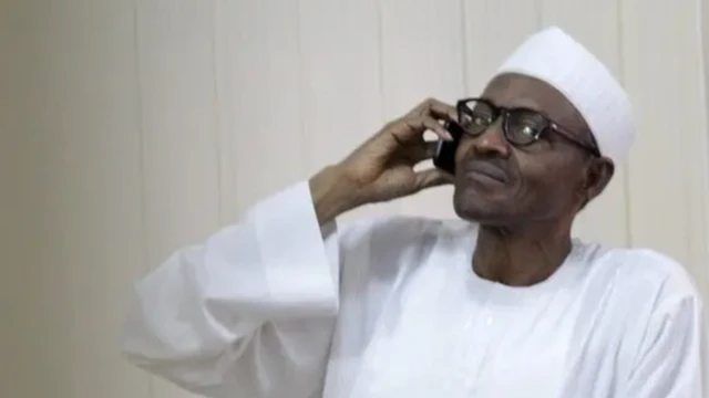 Muhammadu Buhari, vêtu d'un haut blanc à manches longues et d'une casquette blanche, porte un téléphone portable à son oreille.