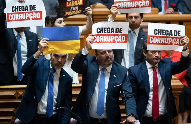 Deputados do Chega seguram cartazes com bandeira da Ucrânia e com frase "chegarealsbet saque recusadocorrupção" durante discursorealsbet saque recusadoLula no Parlamento português