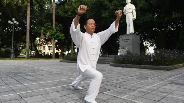 Fotografia mostra homem amarelo fazendo movimentos de arte marcial em uma praça