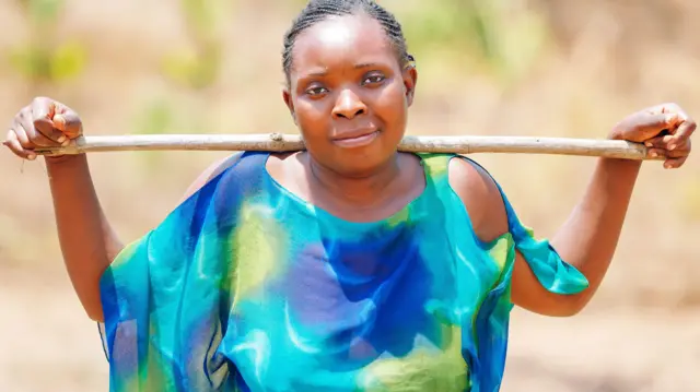 28歲的特瓦利馬村的農民阿比蓋爾·南托韋肖像。她對著鏡頭露出含蓄的微笑，並將一根長木棍橫放在肩胛骨上，雙手搭在木棍上。她身穿一件藍綠相間、飄逸的上衣。