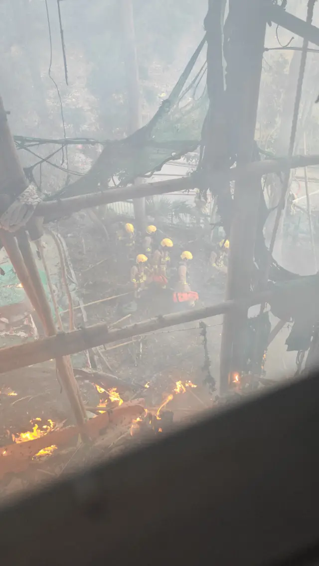 李先生从窗外望出火灾现场，前方有竹棚和被烧掉的棚网，地面是一群消防员。