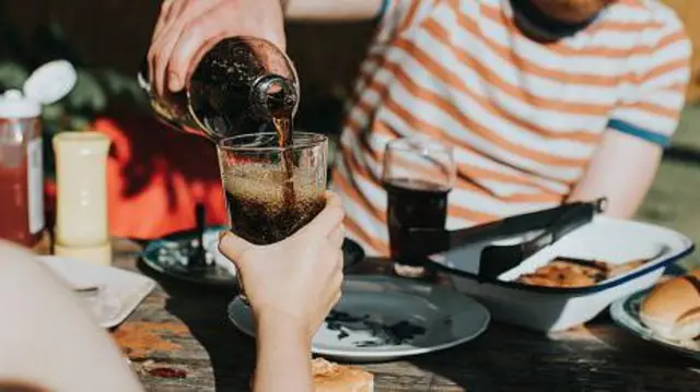 Чоловік за столом наливає у склянку напій