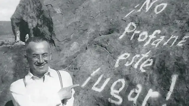 Gonzalo Rojas de joven en una imagen en blanco y negro, junto a una piedra que tiene una inscripción con pintura que pone "¡No profane este lugar!"
