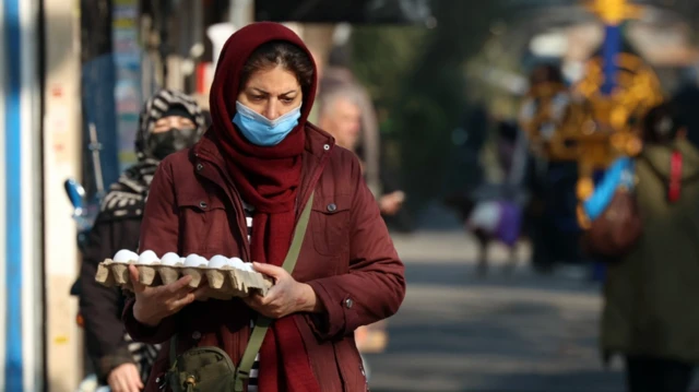 İranlı bir kadın, elinde yumurta kutusuyla Tahran'daki bir sokak pazarında yürüyor.