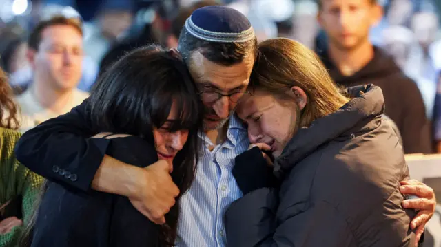 El padre y las dos hermanas de uno de los rehenes israelíes fallecidos se abrazan y lloran.