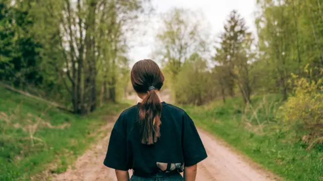 A minor with her back turned on a dirt road.
