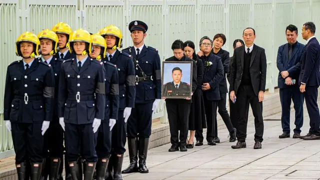 Relatives of firefighter Ho Wai-ho, who died in the deadly fire at the Wang Fuk Court residential estate in Tai Po district, hold his portrait during his burial at Gallant Garden in Hong Kong on December 19, 2025. 