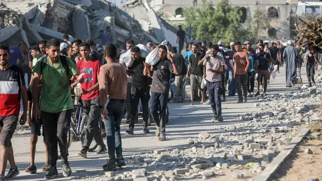 Des Palestiniens traversent à pied le corridor de Netzarim, dans le centre de Gaza, transportant des colis d'aide reçus d'un point de distribution d'aide basé aux États-Unis et mis en place par la Fondation humanitaire de Gaza (GHF), le 26 juin 2025, dans le cadre de la crise humanitaire qui fait suite à 20 mois de conflit avec Israël.