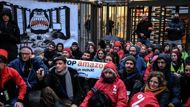 نشكاء محتجّون على "الجمعة السوداء" يغلقون مدخل المقر الرئيسي لشركة أمازون في فرنسا رافعين لافتة كتب عليها" أوقفوا أمازون وعالمها".